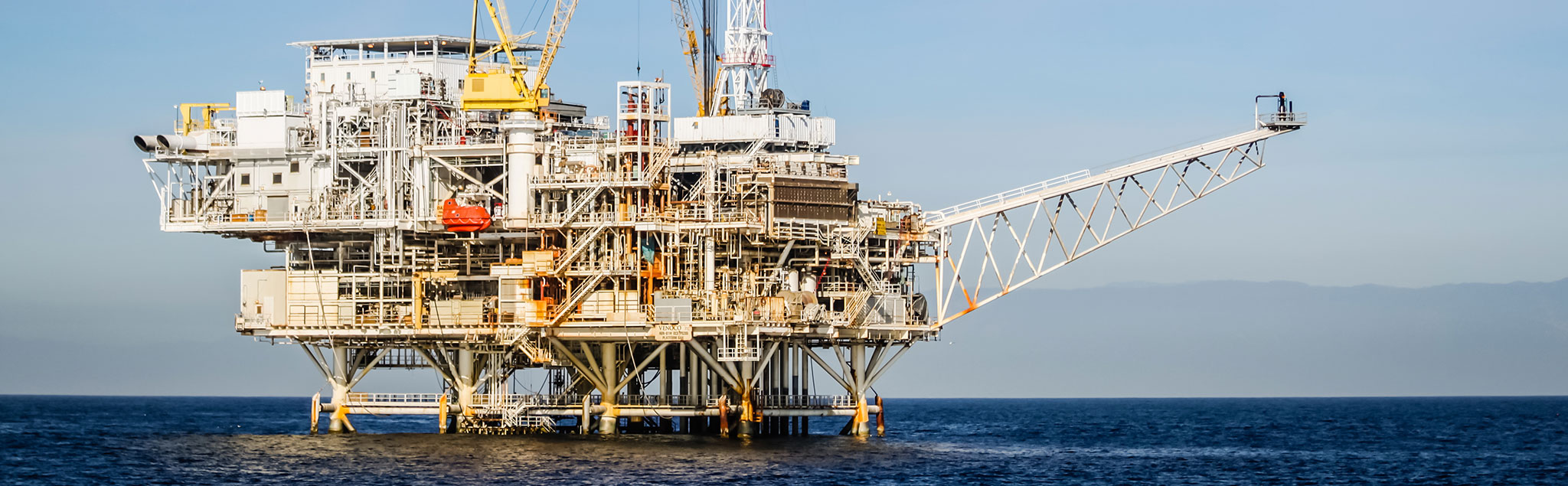 Zu sehen ist eine Bohrinsel. Das Meer ist ruhig und der Himmel blau.