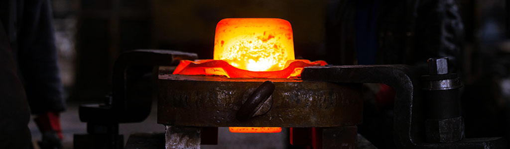 Der Focus liegt auf einem rot-orange glühenden Knüppel (Metallkörper) der sich in einem Gesenk befindet.